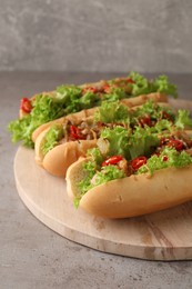 Photo of Tasty hot dogs with chili, lettuce and sauce on grey textured table, closeup