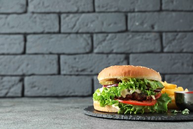 Photo of Delicious burger with beef patty, tomato sauce and french fries on grey table, space for text