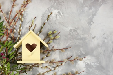 Photo of Stylish bird house and fresh pussy willow branches on light grey stone background, flat lay. Space for text