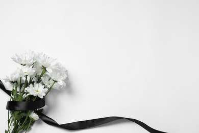 Photo of Beautiful chrysanthemum flowers and black ribbon on white background, top view with space for text. Funeral symbols