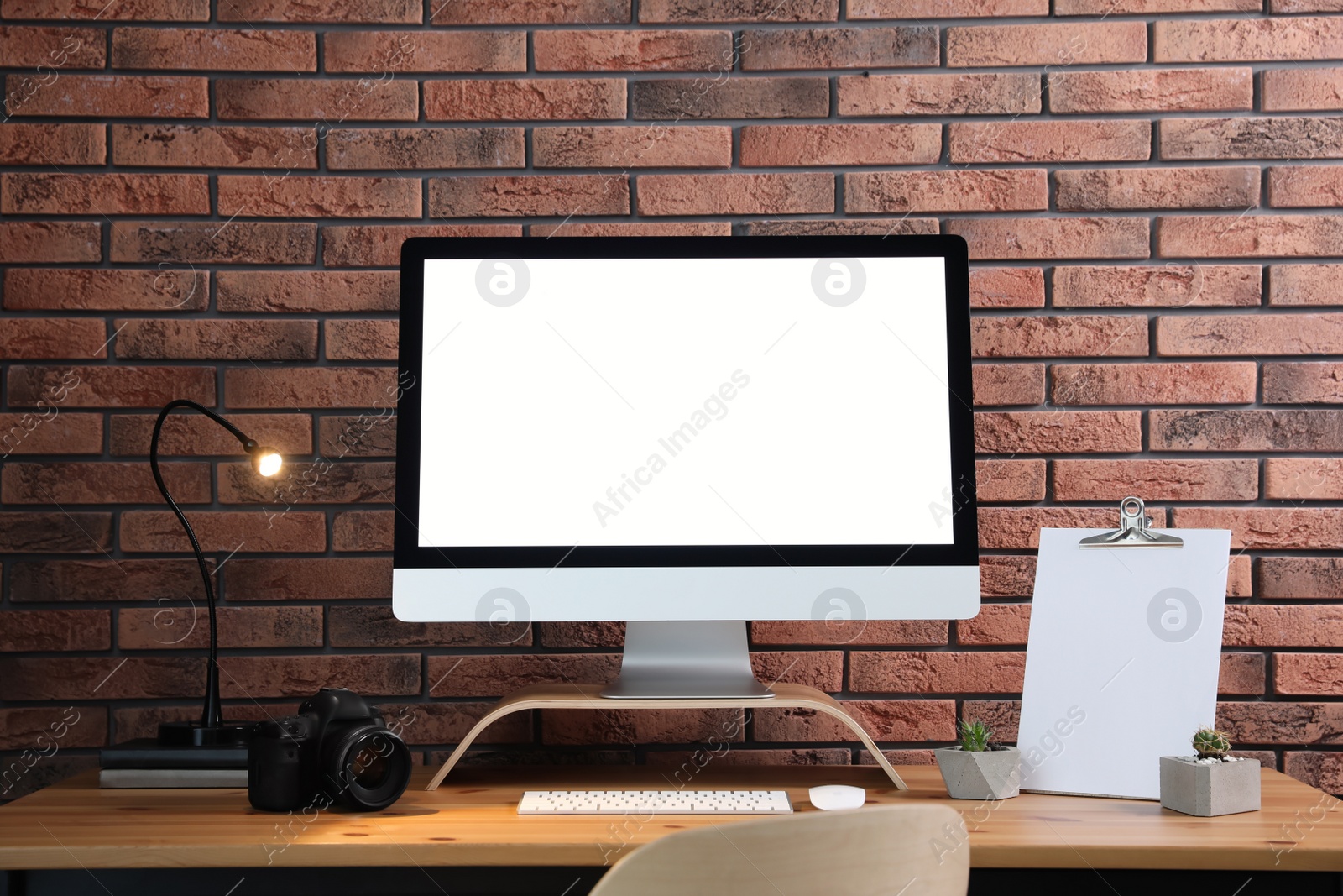 Photo of Comfortable workplace with modern computer on wooden table near brick wall. Space for text