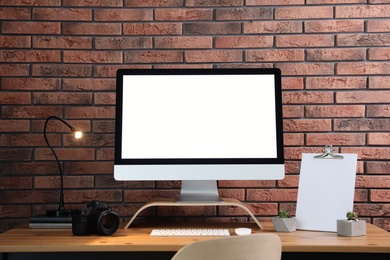 Comfortable workplace with modern computer on wooden table near brick wall. Space for text