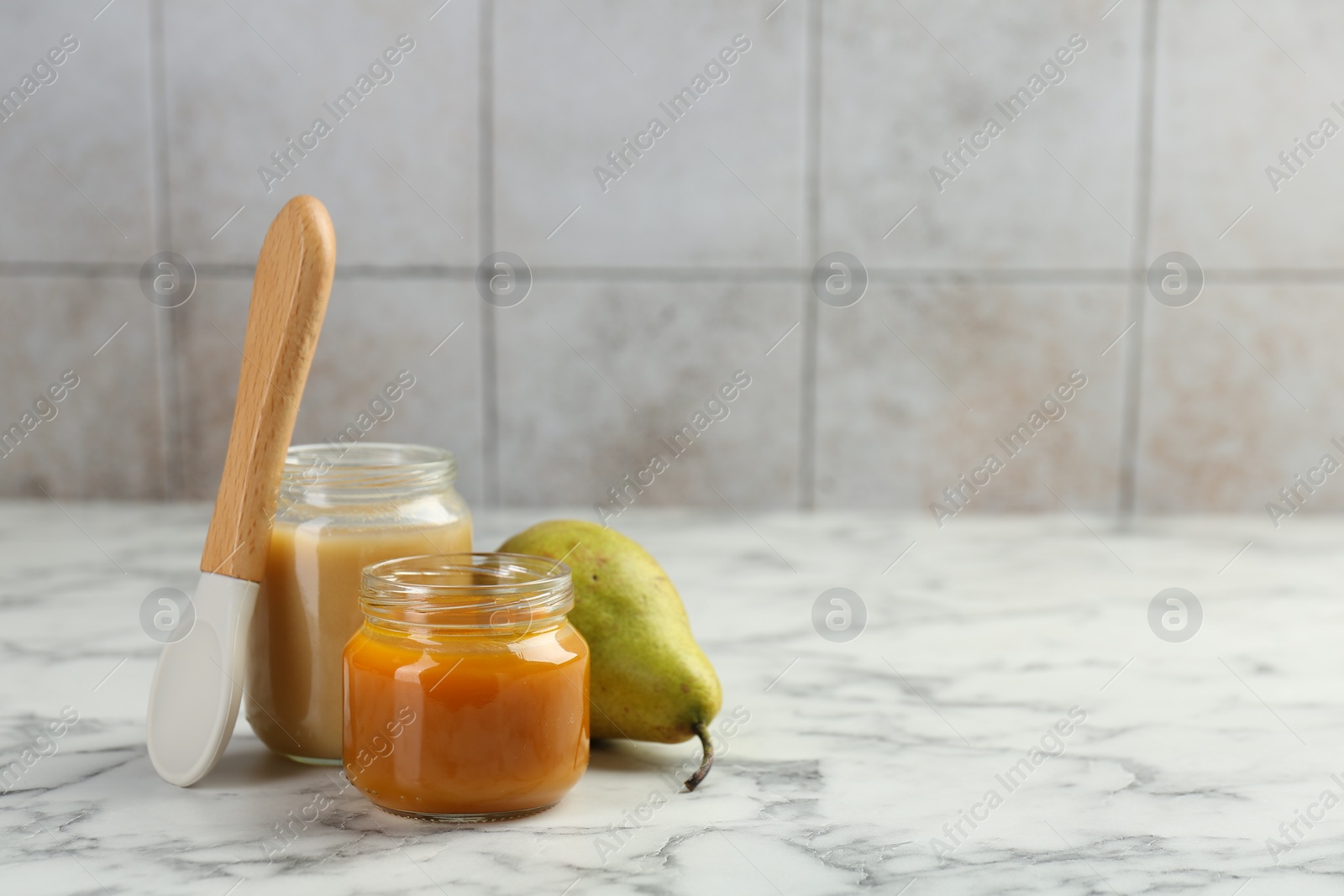 Photo of Tasty baby food in jars, pear and spoon on white marble table. Space for text