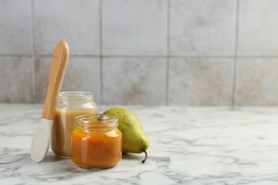 Photo of Tasty baby food in jars, pear and spoon on white marble table. Space for text