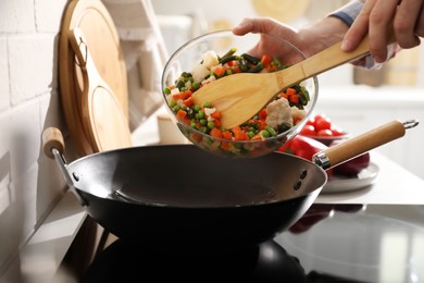 Photo of Man pouring mix of fresh vegetables into frying pan, closeup