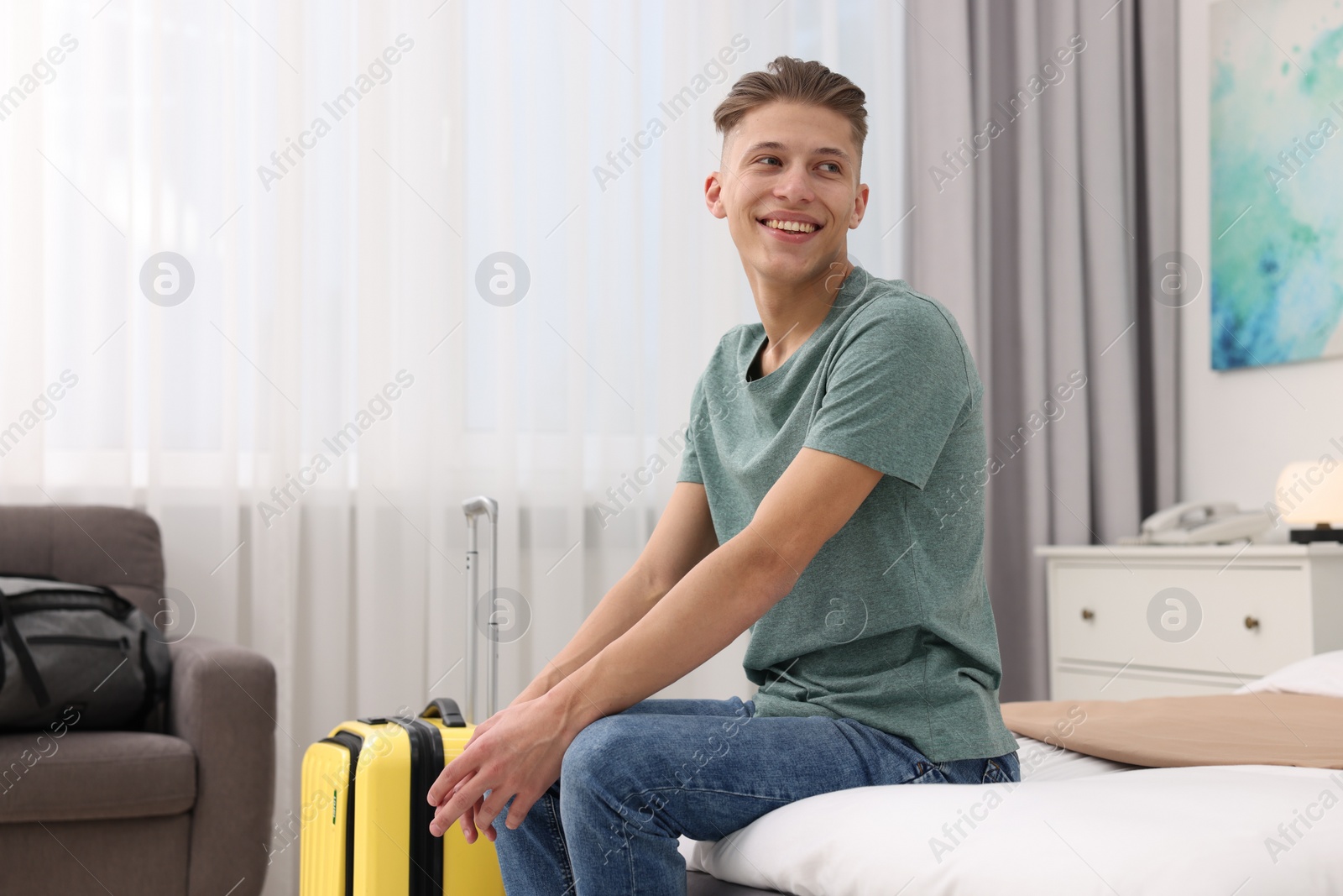 Photo of Smiling guest with suitcase relaxing on bed in stylish hotel room. Space for text