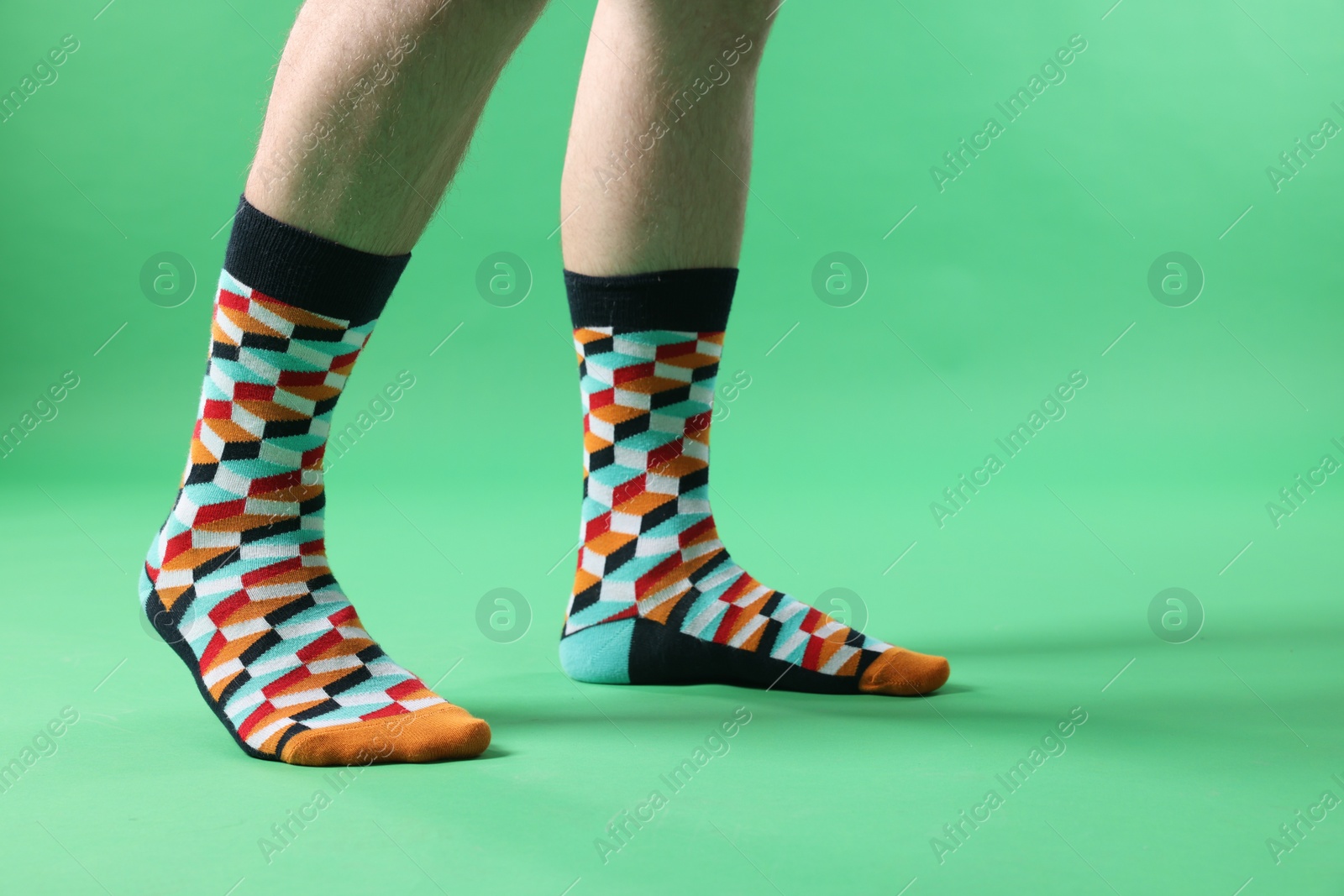 Photo of Man in stylish colorful socks on light green background, closeup. Space for text