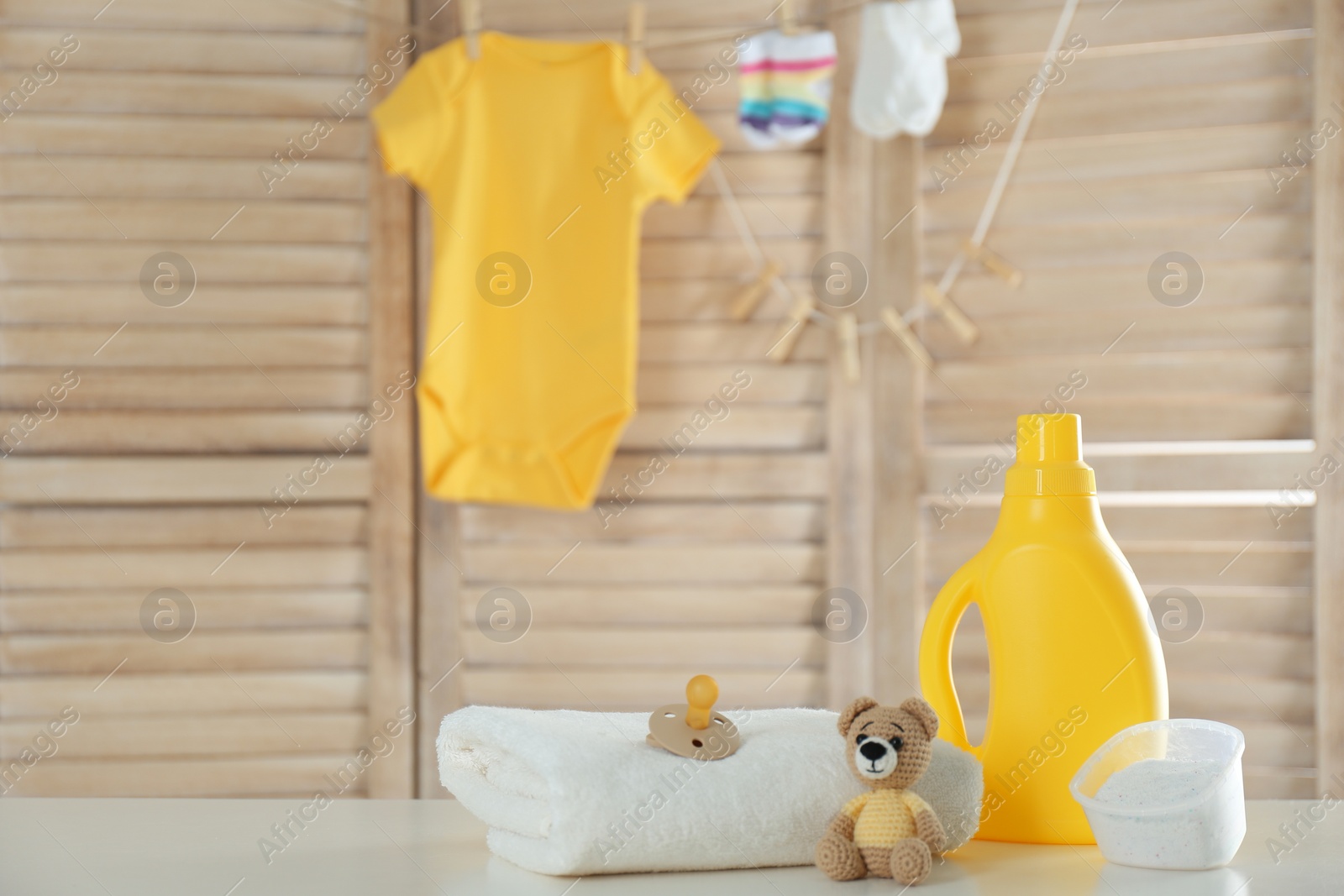 Photo of Fresh baby towel, toys, bottle of detergent and washing powder on wooden table