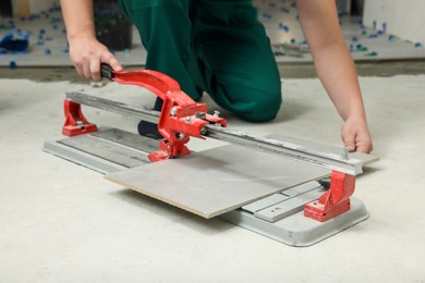 Photo of Worker using manual tile cutter on floor, closeup