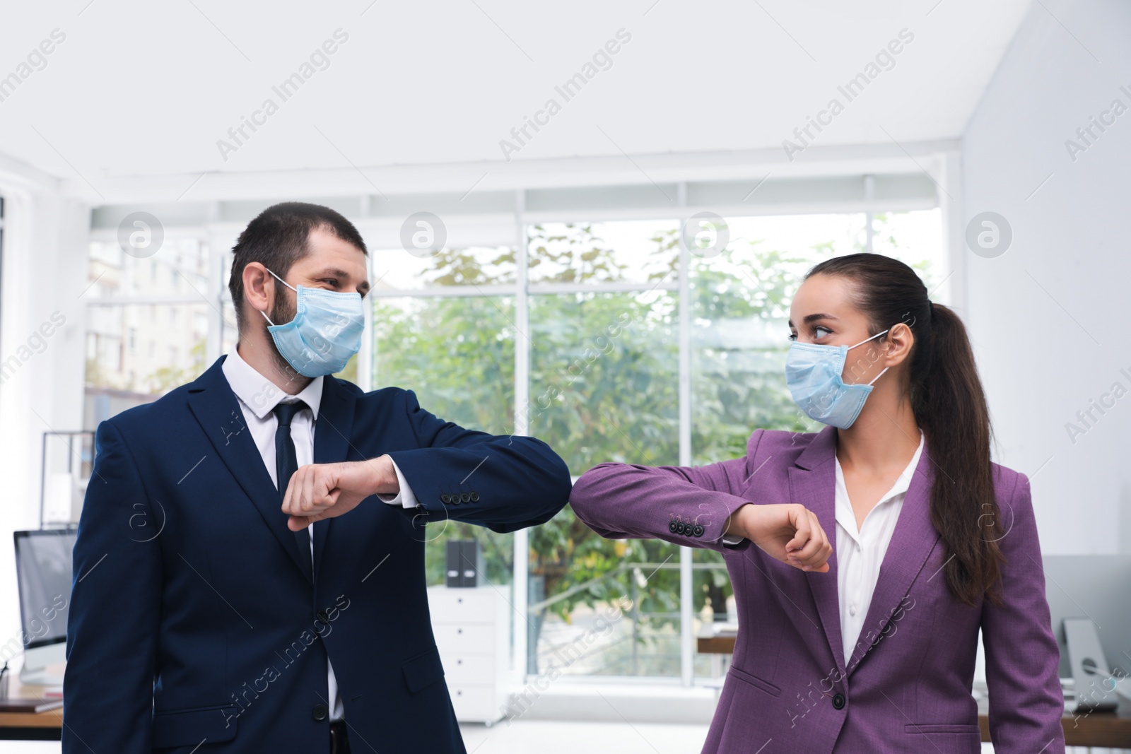 Photo of Office employees in masks greeting each other by bumping elbows at workplace