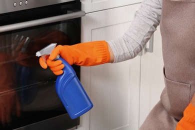 Photo of Woman cleaning oven with detergent in kitchen, closeup