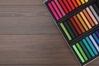 Photo of Set of colorful pastels in box on wooden table, top view with space for text. Drawing materials