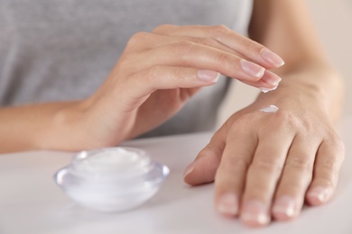 Photo of Young woman applying hand cream at table, closeup