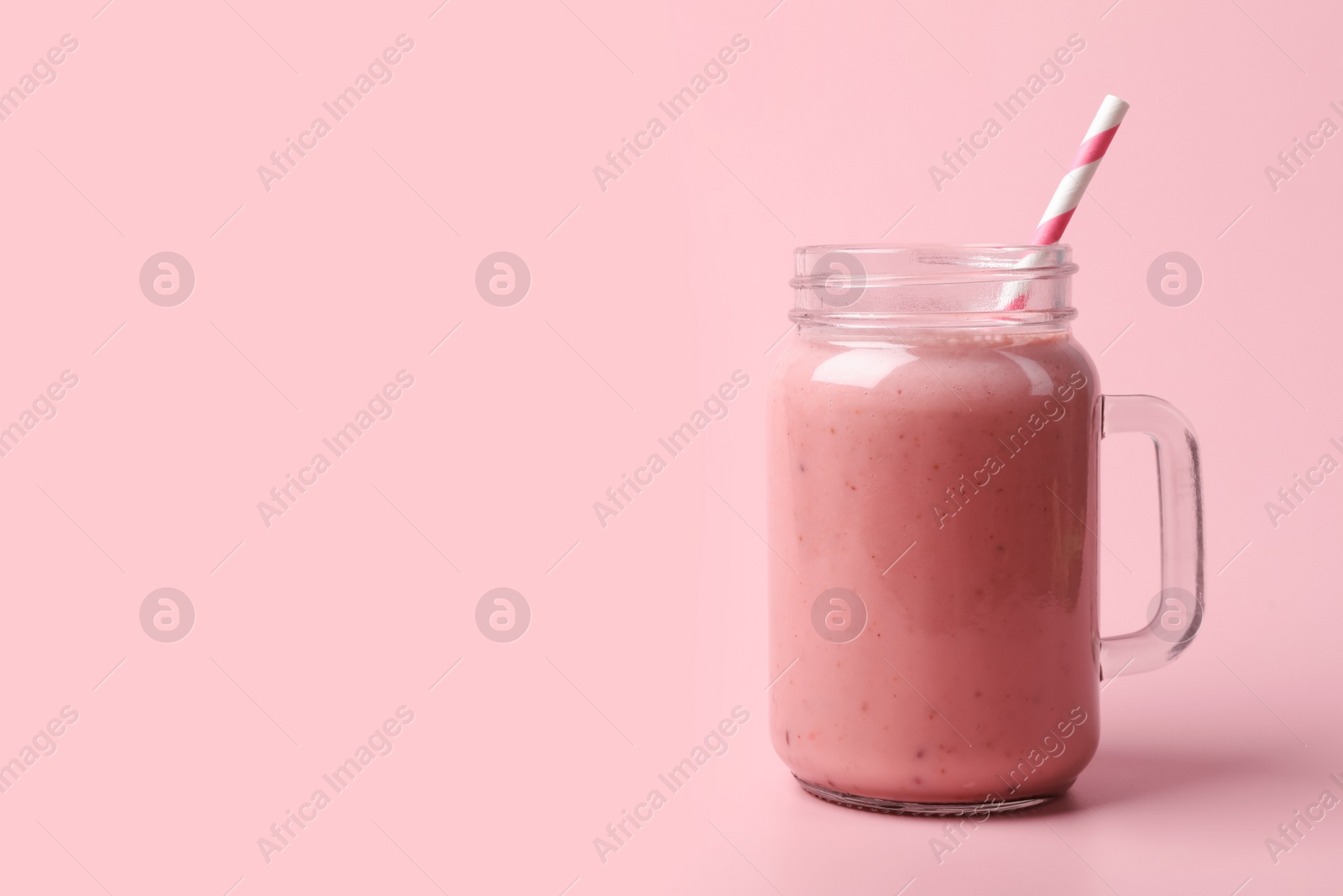 Photo of Mason jar with delicious berry smoothie on pink background. Space for text