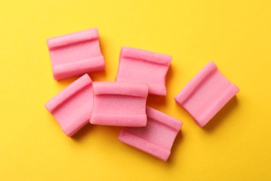 Tasty pink chewing gums on yellow background, flat lay