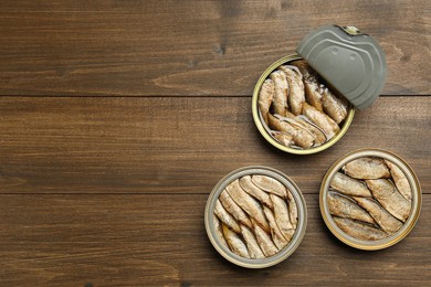 Photo of Open tin cans of sprats on wooden table, flat lay. Space for text