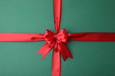 Photo of Red satin ribbon with bow on green background, top view