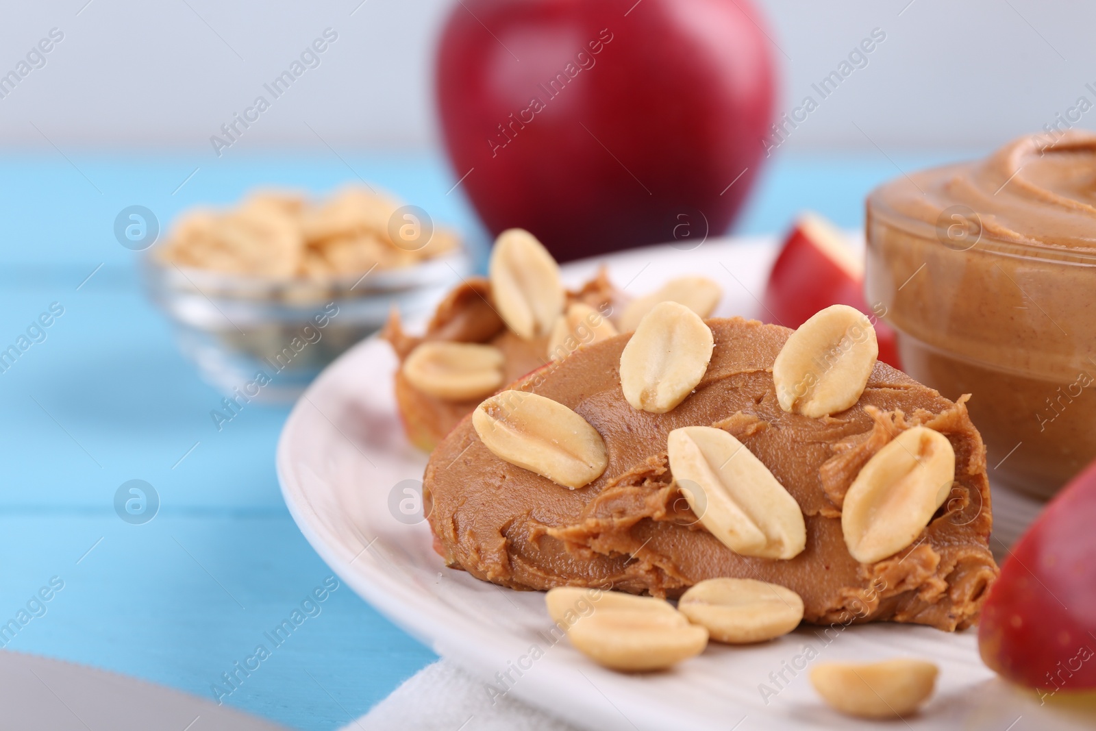 Photo of Slice of fresh apple with peanut butter and nuts on light blue wooden table, closeup