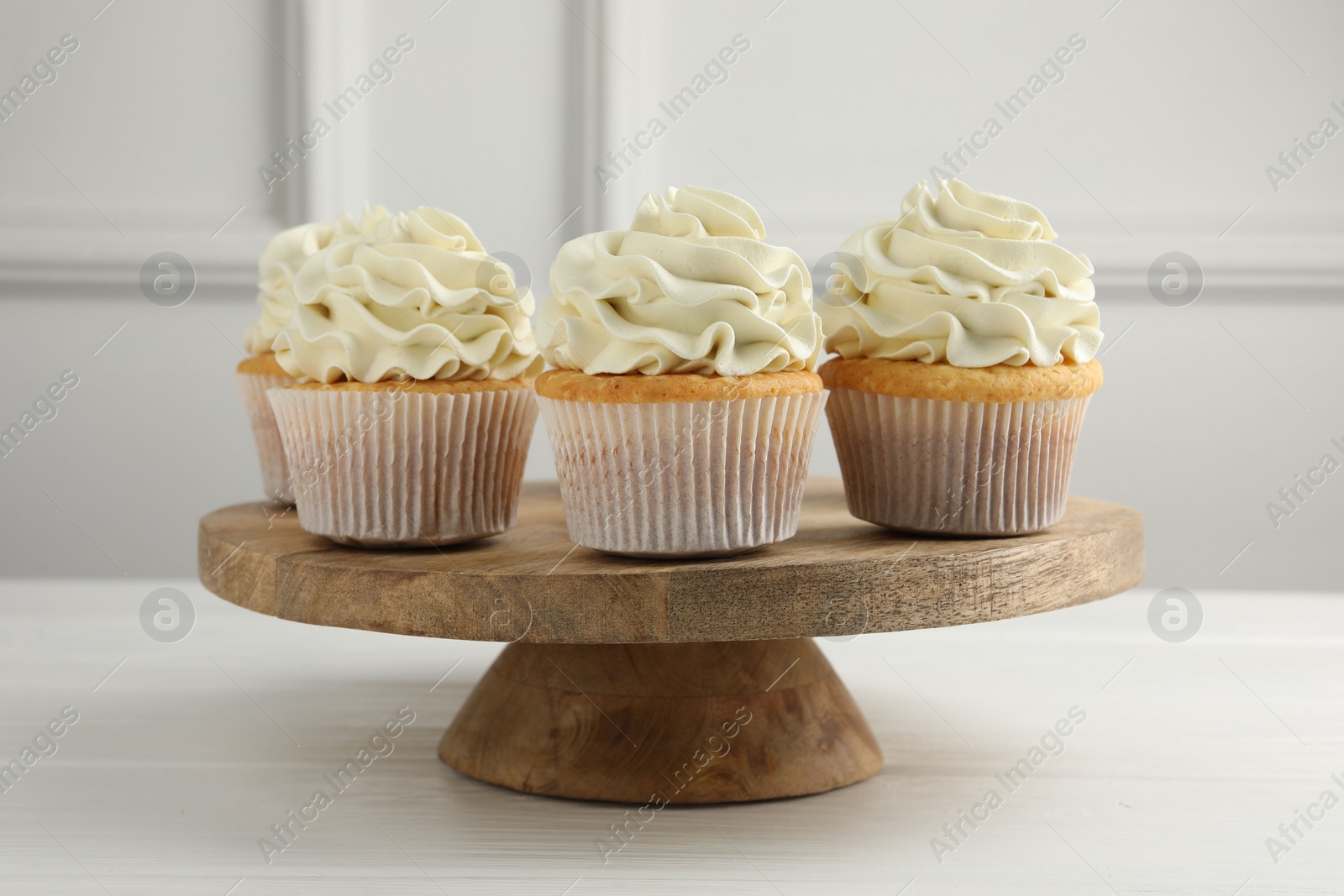 Photo of Tasty vanilla cupcakes with cream on white wooden table