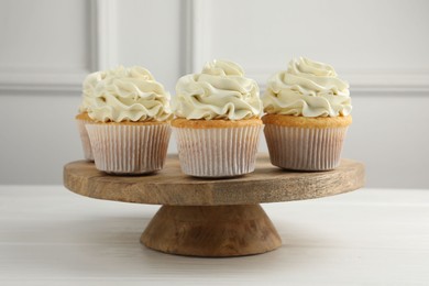 Tasty vanilla cupcakes with cream on white wooden table