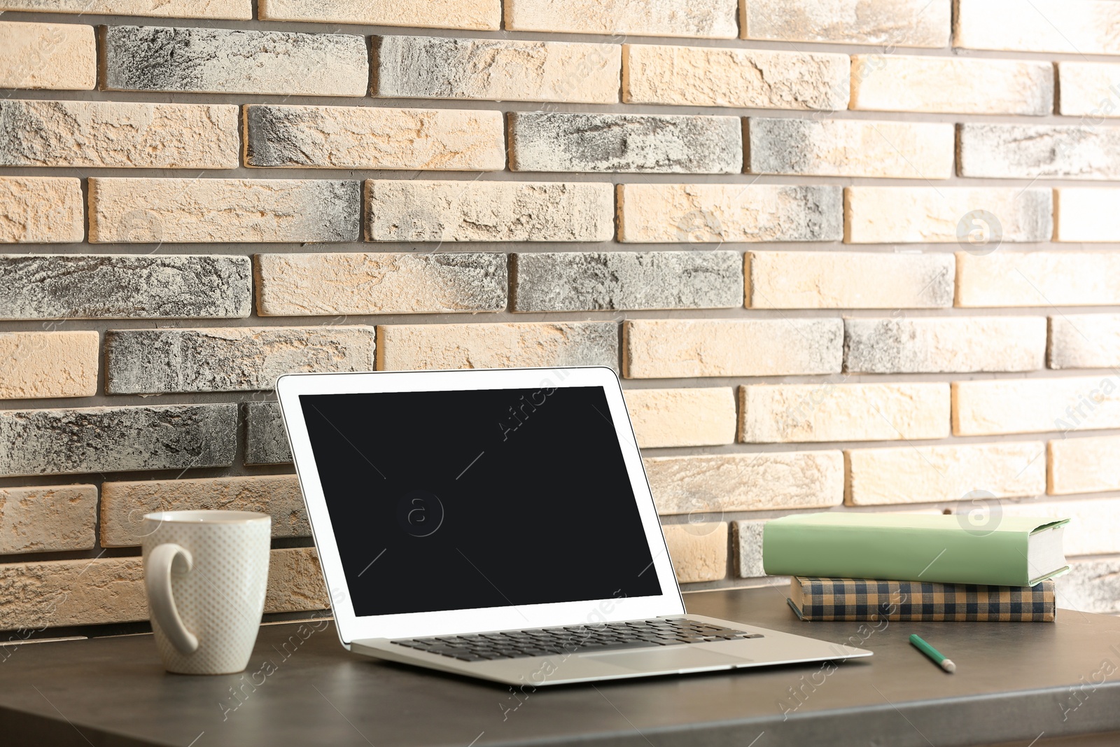 Photo of Modern laptop on table against brick wall. Mock up with space for text