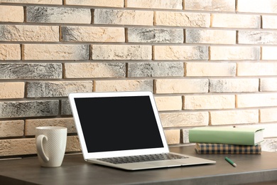 Modern laptop on table against brick wall. Mock up with space for text