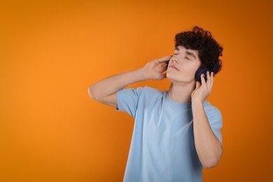 Photo of Teenage boy listening music with headphones on orange background. Space for text