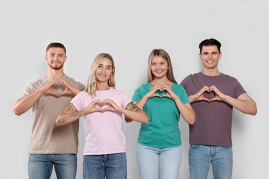 Photo of Happy volunteers making hearts with their hands on light background