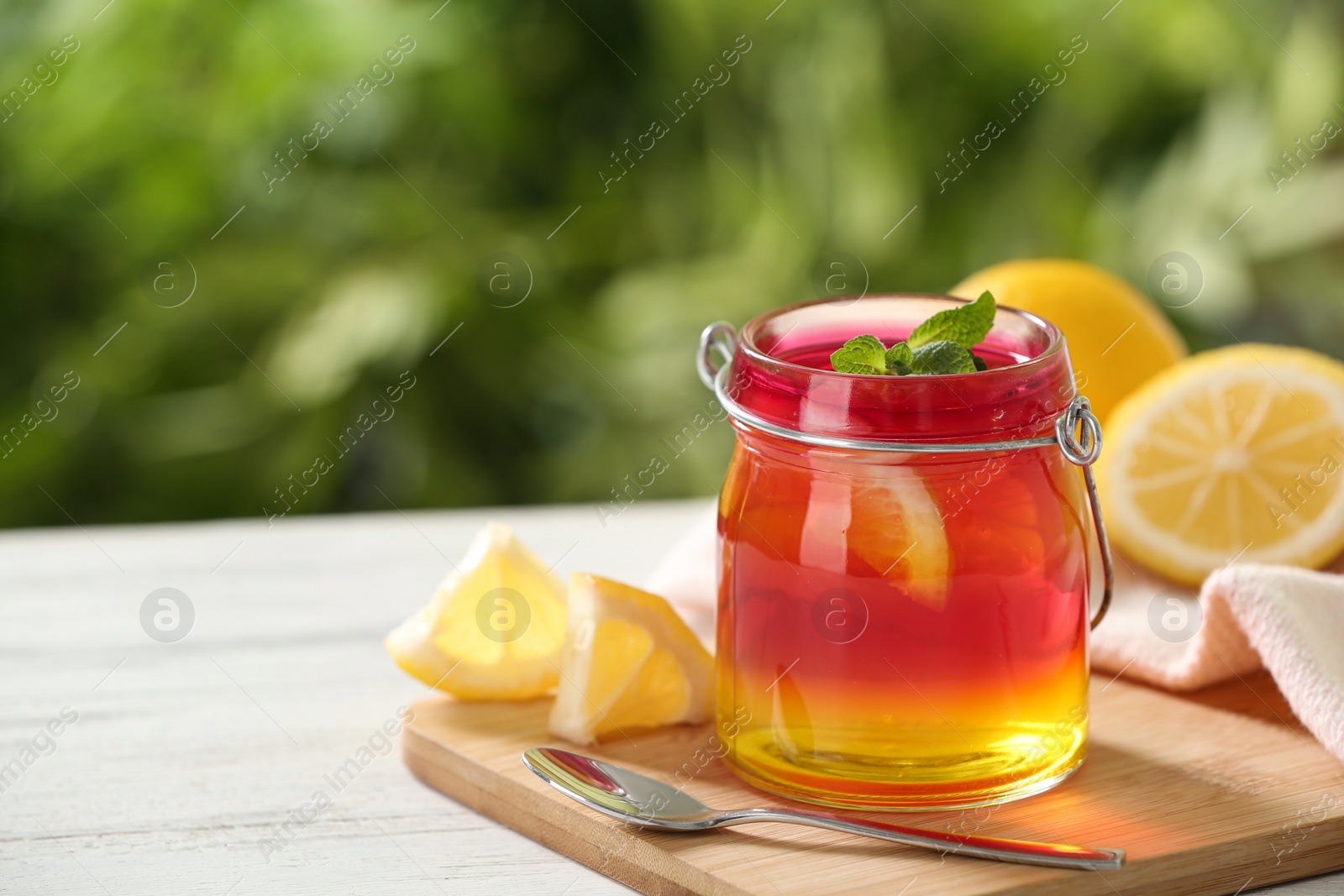 Photo of Board with jar of colorful jelly, spoon and lemon slices on white table. Space for text