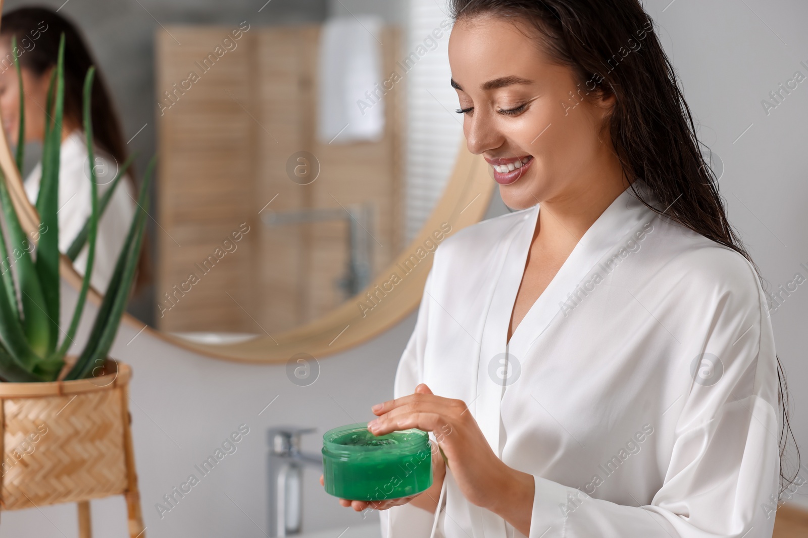 Photo of Young woman holding jar of aloe hair mask in bathroom. Space for text