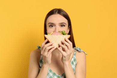 Photo of Young woman eating tasty sandwich on yellow background