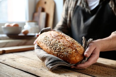 Photo of Man holding loaf of fresh bread at wooden table indoors, closeup