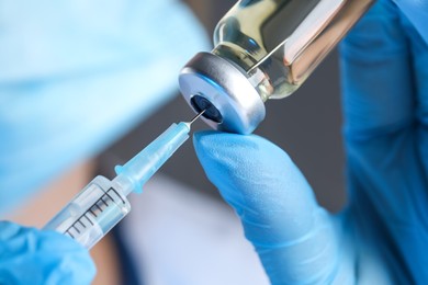 Doctor filling syringe with medication from glass vial, closeup