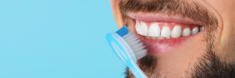 Image of Man brushing his teeth with plastic toothbrush on light blue background, closeup. Banner design with space for text