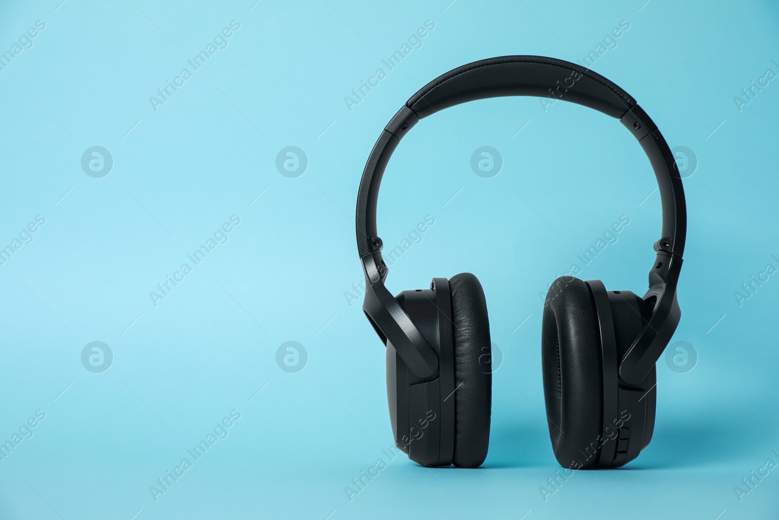 Photo of Modern wireless headphones on light blue background. Space for text