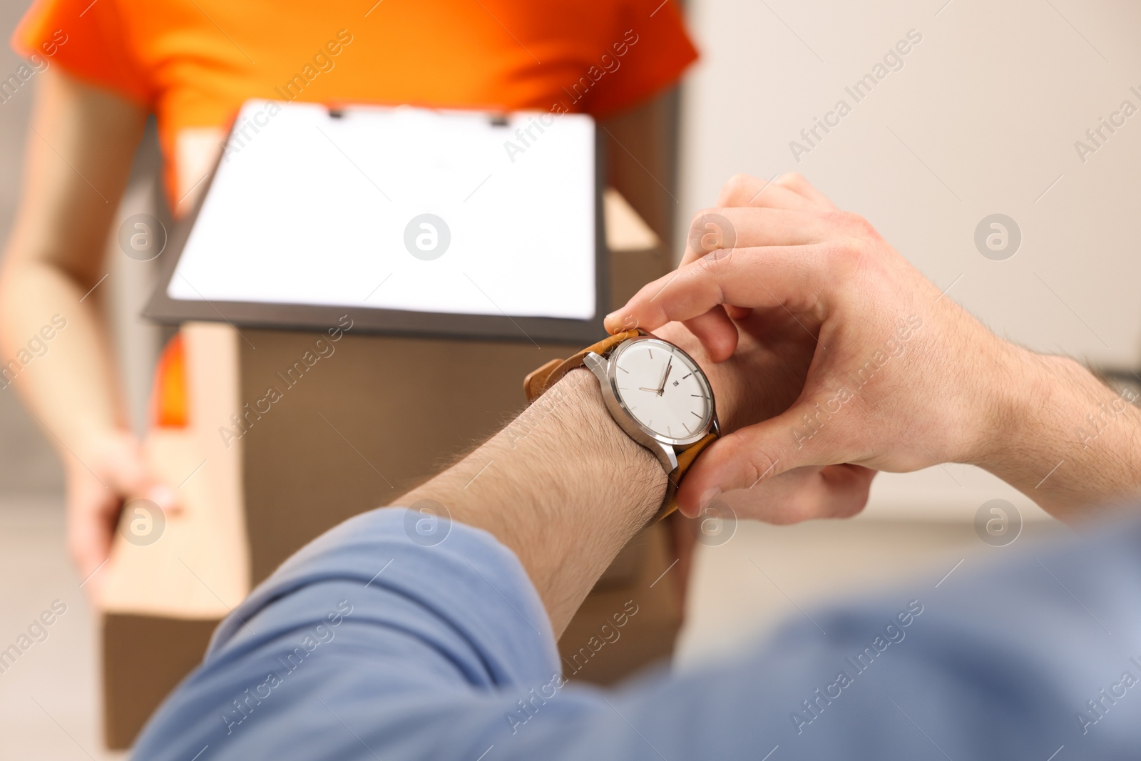 Photo of Closeup view of man checking time near courier with parcels indoors