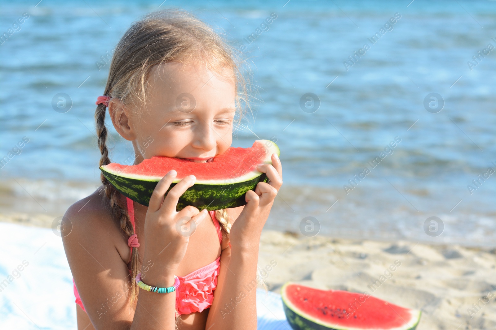 Photo of Cute little girl eating juicy watermelon on beach, space for text