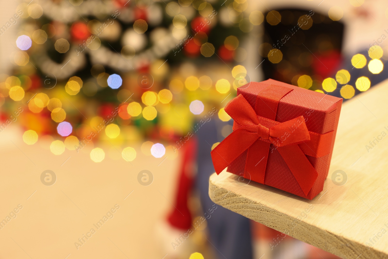 Photo of Red gift box on wooden shelf against blurred festive lights, space for text. Christmas celebration