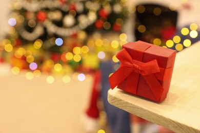 Photo of Red gift box on wooden shelf against blurred festive lights, space for text. Christmas celebration