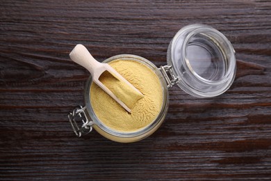 Scoop and glass jar with granulated brewer`s yeast on wooden table, top view