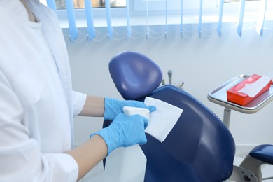 Photo of Professional dentist in white coat cleaning workplace  with antiseptic indoors, closeup