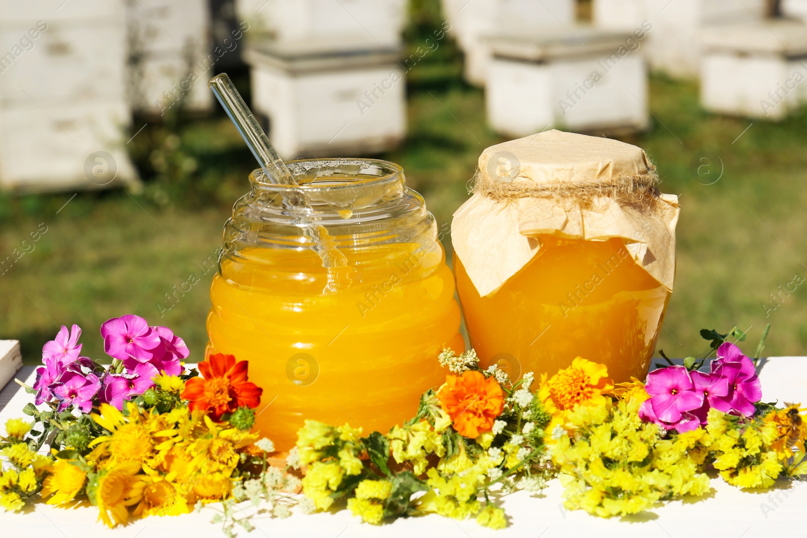 Photo of Delicious fresh honey and beautiful flowers on white wooden table in garden