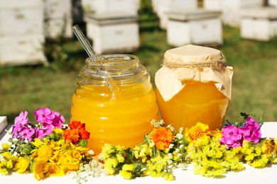Delicious fresh honey and beautiful flowers on white wooden table in garden