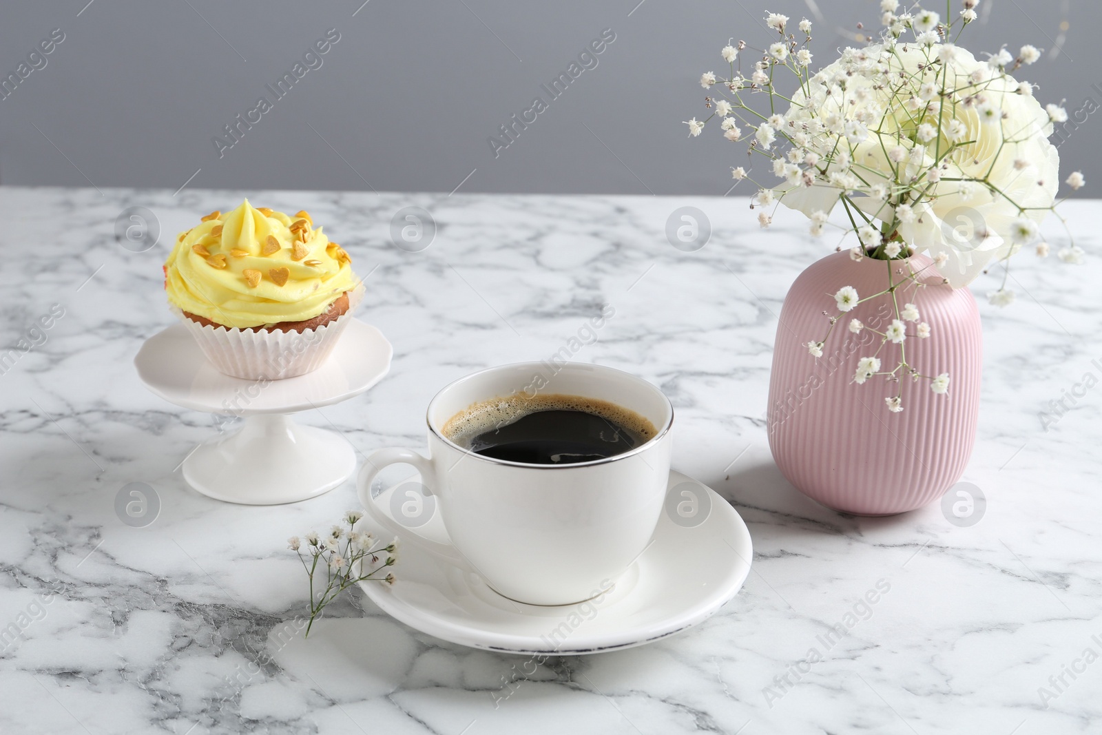 Photo of Delicious cupcake with yellow cream, coffee and flowers on white marble table