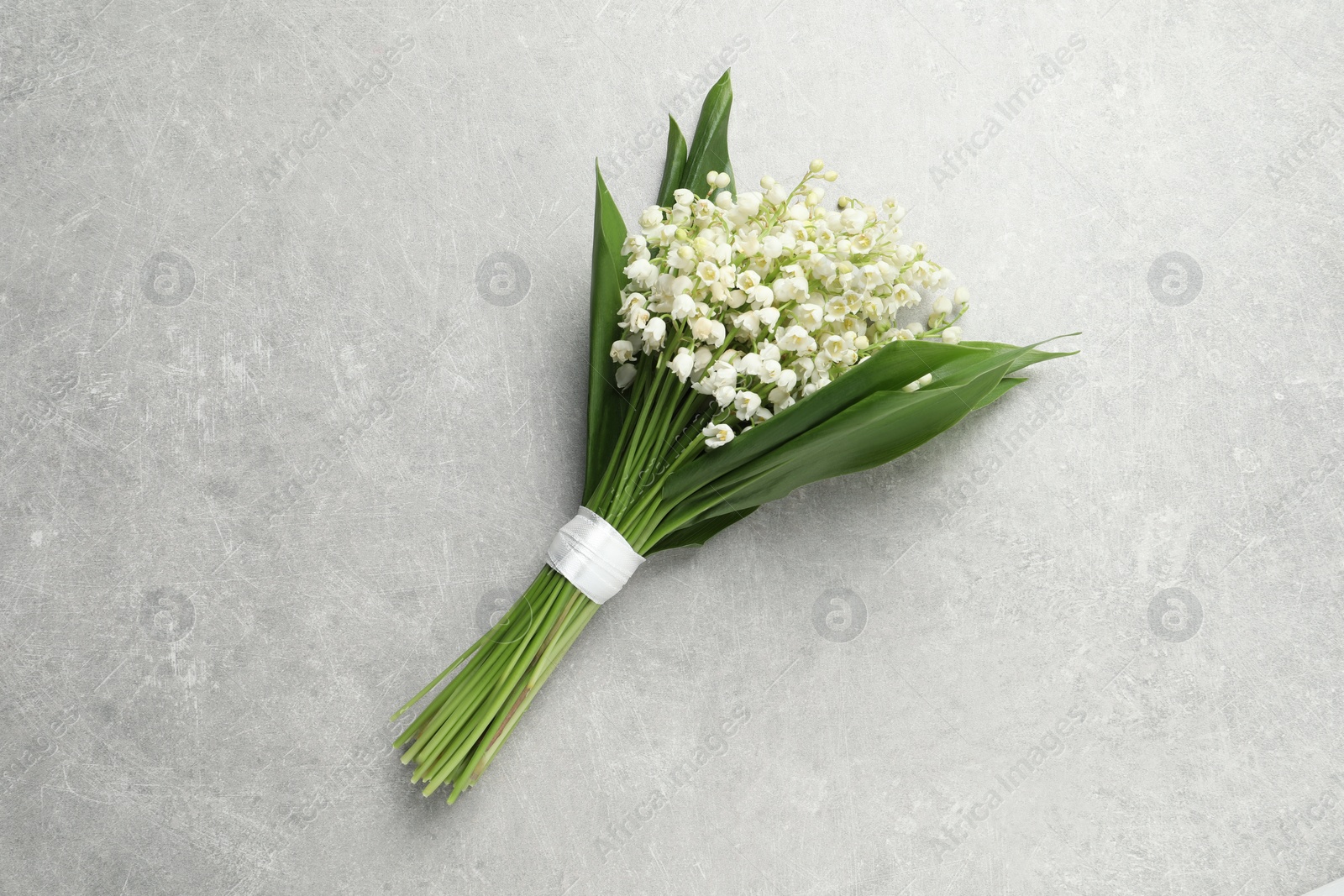 Photo of Beautiful lily of the valley bouquet on grey table, top view
