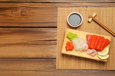Photo of Delicious sashimi set of salmon and shrimps served with funchosa, lemon, lettuce and soy sauce on wooden table, top view. Space for text