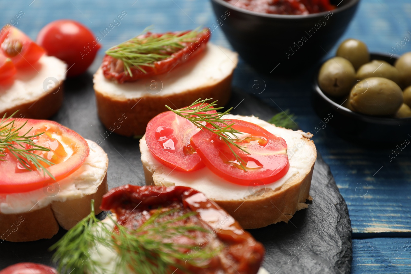 Photo of Delicious bruschettas with ricotta cheese, tomatoes, dill and olives on blue wooden table, closeup