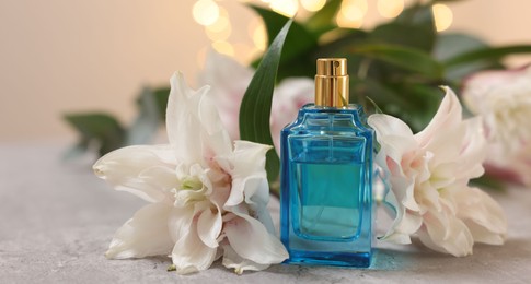 Photo of Bottle of perfume and beautiful lily flowers on table against beige background with blurred lights, closeup