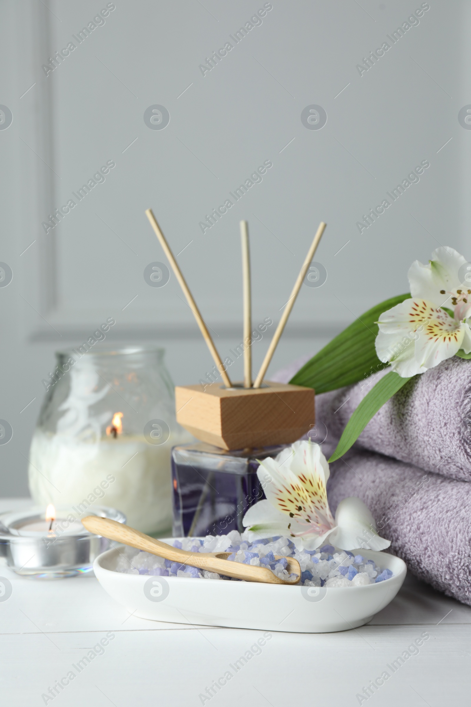 Photo of Spa composition. Towels, burning candles, reed air freshener, sea salt and beautiful flowers on white wooden table, closeup