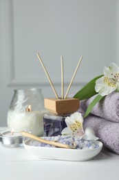 Photo of Spa composition. Towels, burning candles, reed air freshener, sea salt and beautiful flowers on white wooden table, closeup